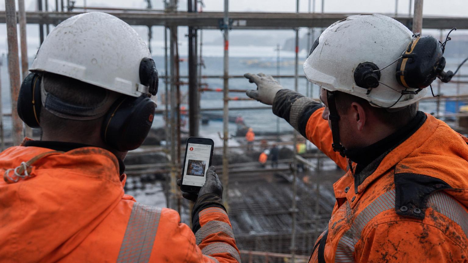 To byggearbeidere på stillas registrerer avvik på mobil – avvikshåndtering på byggeplass